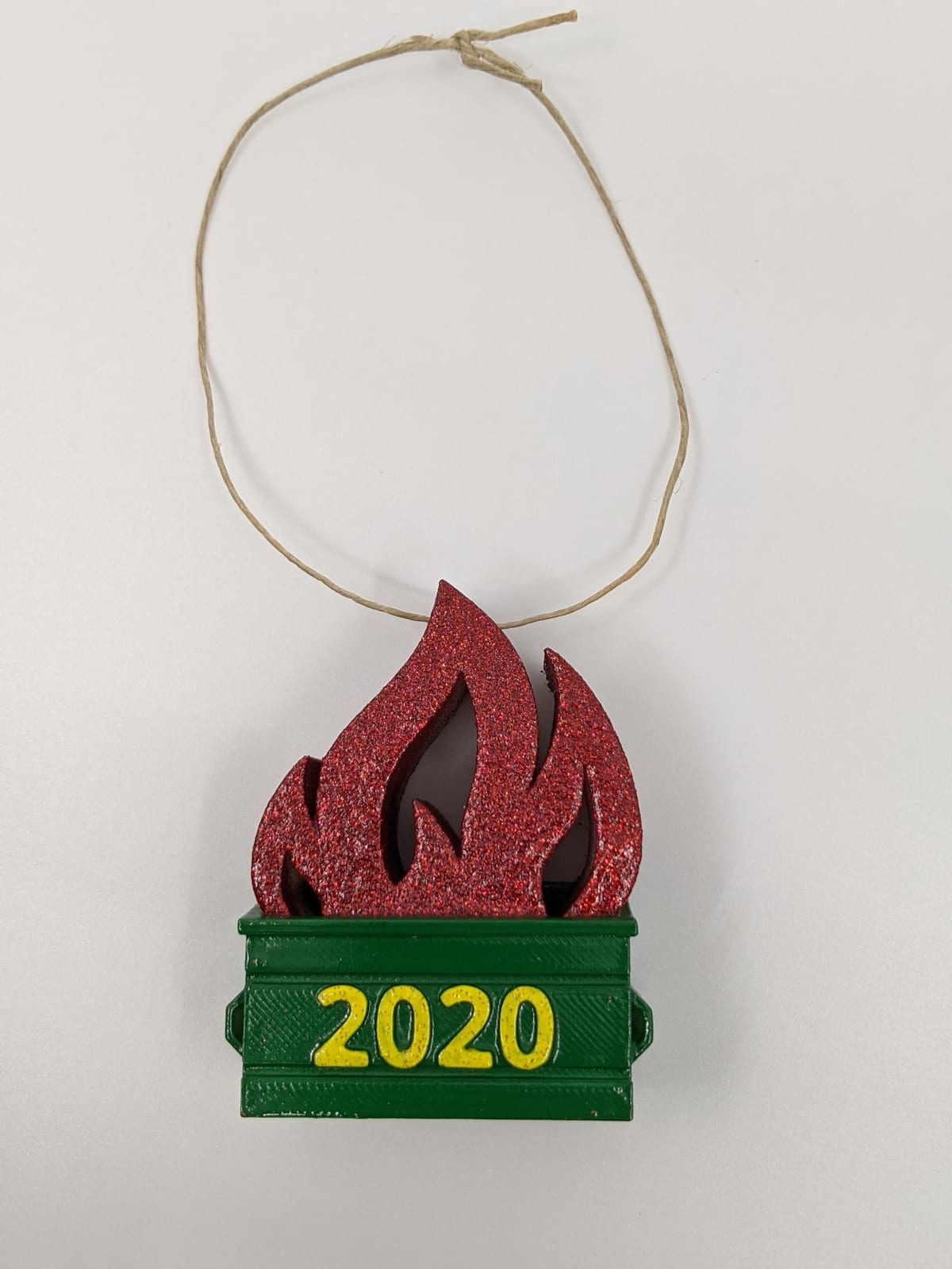 3D-printed dumpster fire ornament — a green dumpster reading 2020 with red glitter flames and a string hanger