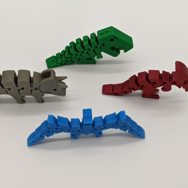 Four articulated 3D-printed dinosaurs — a green T-rex, gray triceratops, red raptor and blue stegosaurus
