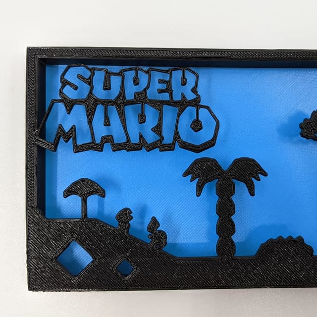 Black layered Super Mario shadow box on blue with clouds, a palm and the classic landscape
