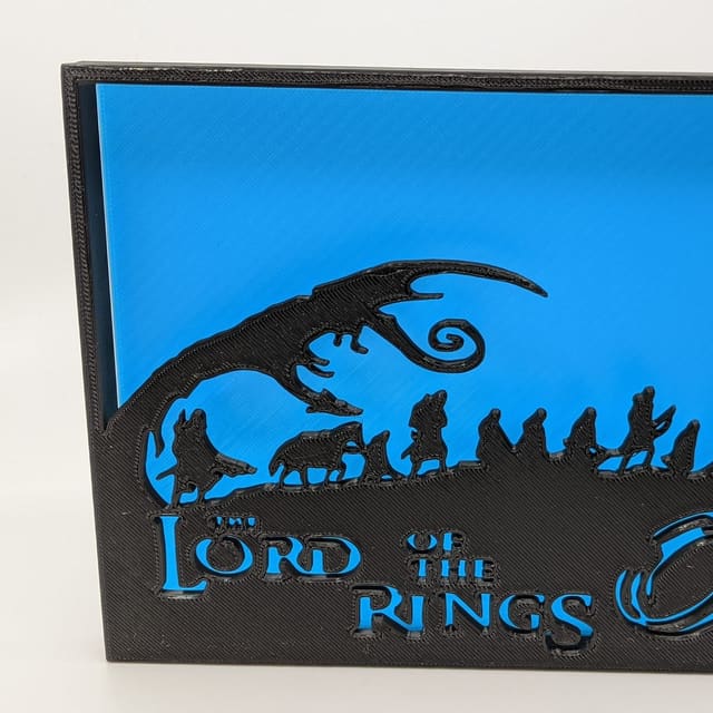 Black Lord of the Rings shadow box on blue — the Fellowship in silhouette under the title and the One Ring
