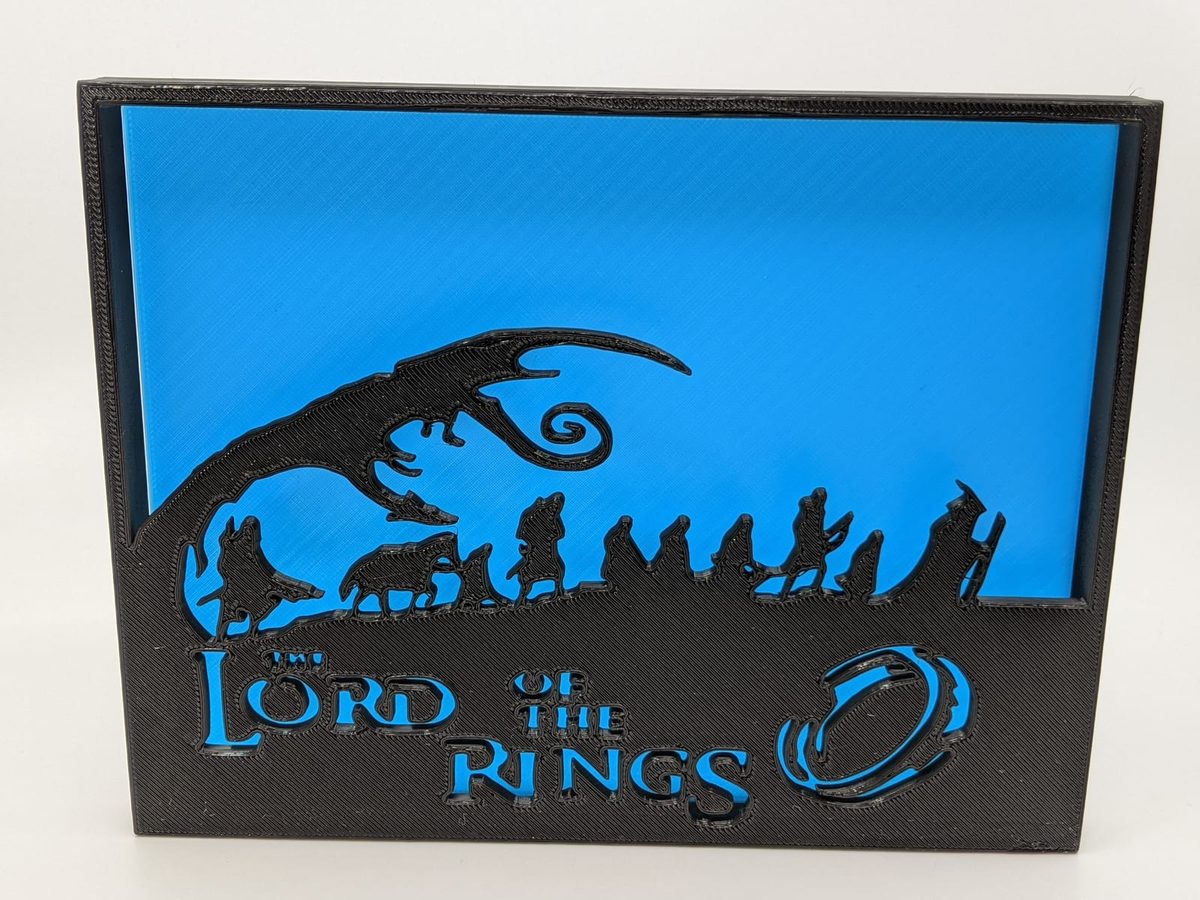Black Lord of the Rings shadow box on blue — the Fellowship in silhouette under the title and the One Ring