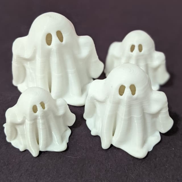 Four small white 3D-printed ghosts with cut-out eyes