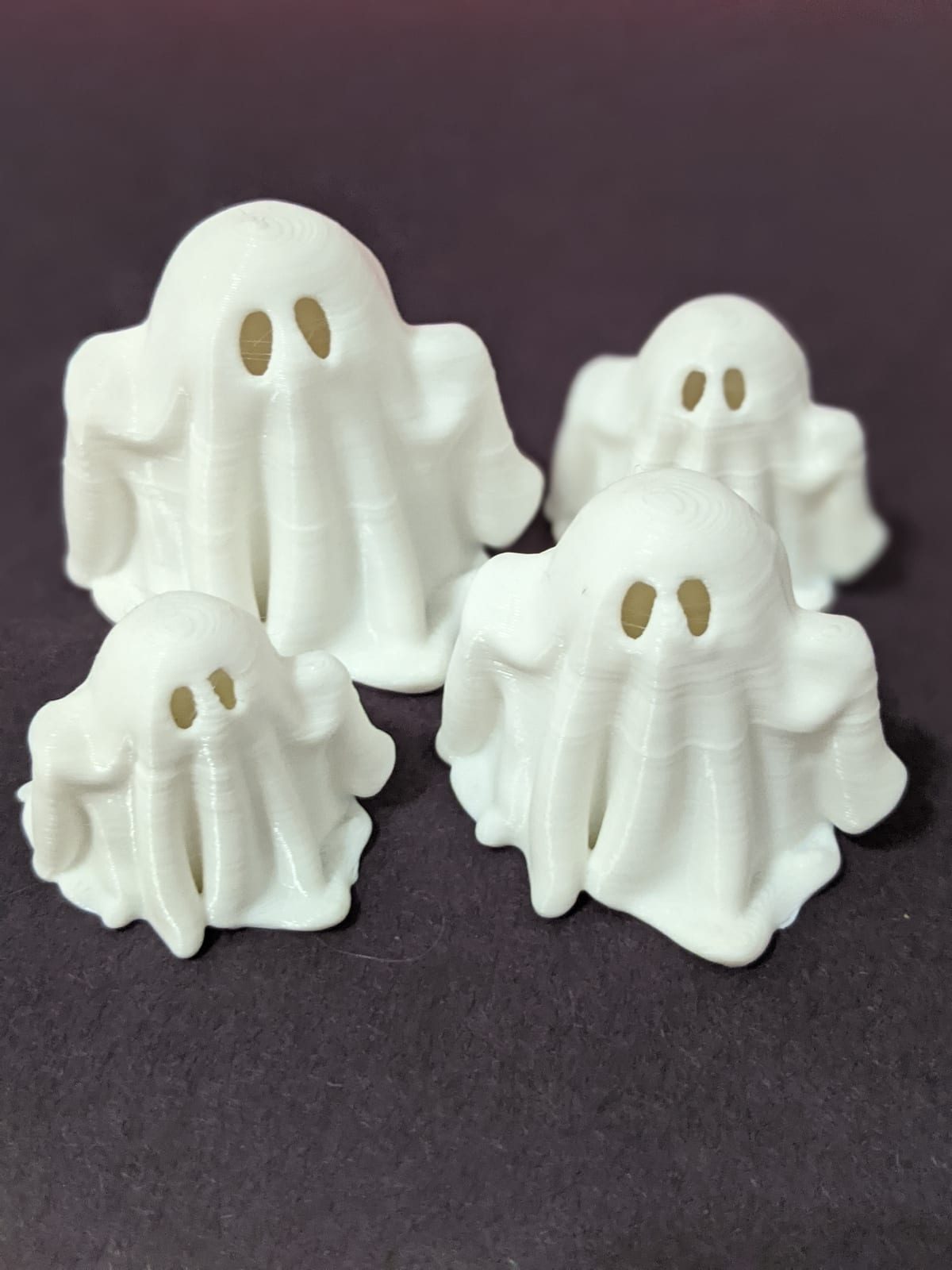 Four small white 3D-printed ghosts with cut-out eyes