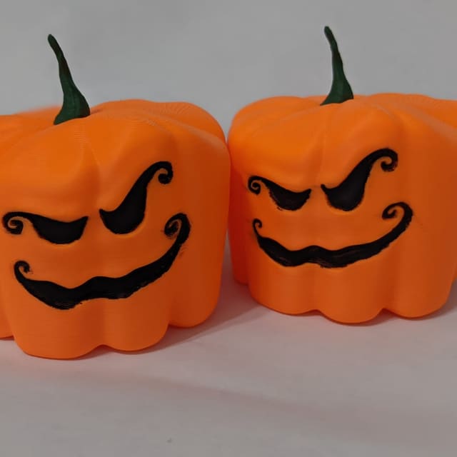 Two orange 3D-printed jack-o'-lantern boxes with grinning faces and green stem lids