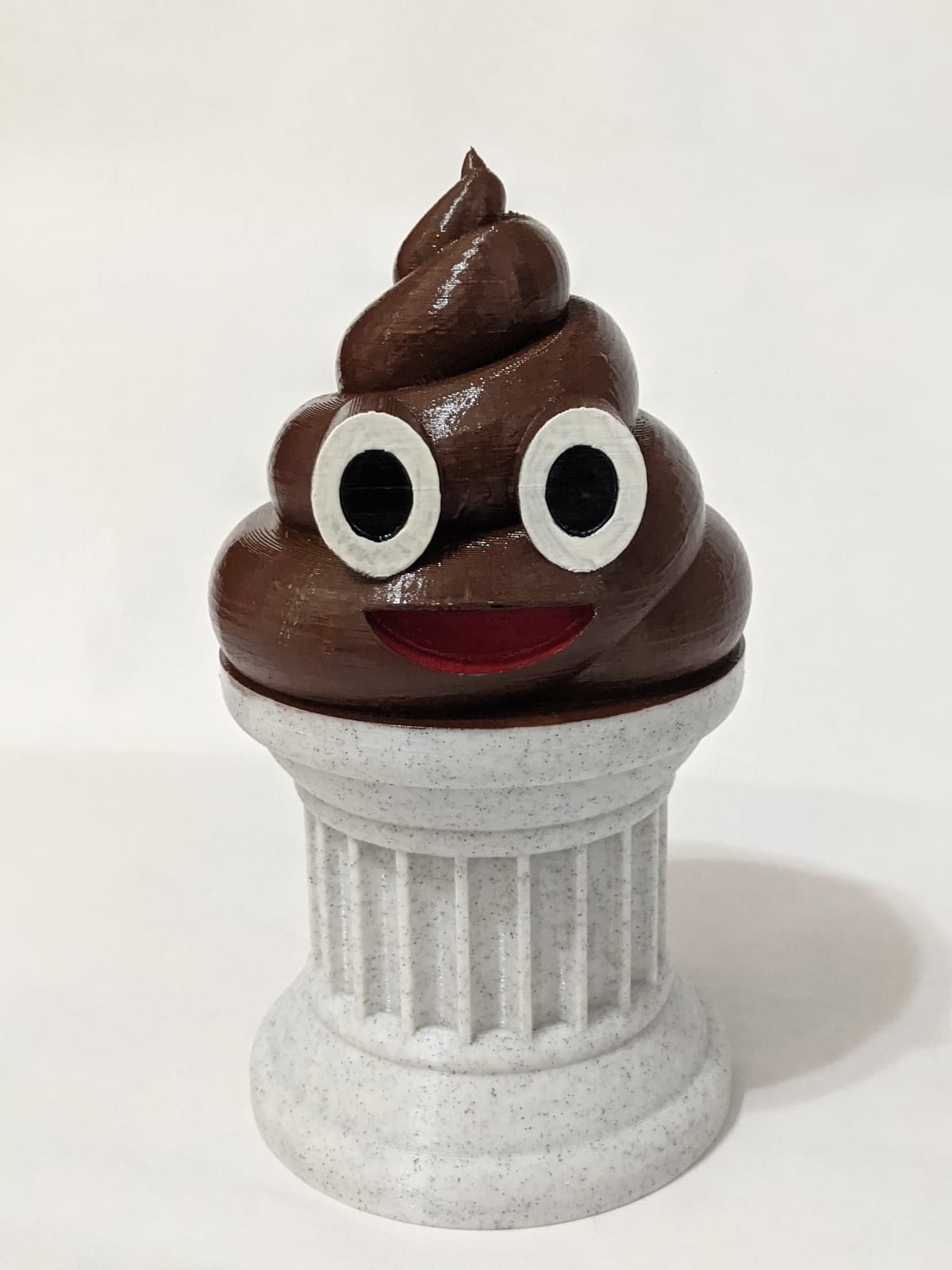 A smiling brown 3D-printed poop emoji displayed on a white classical pedestal
